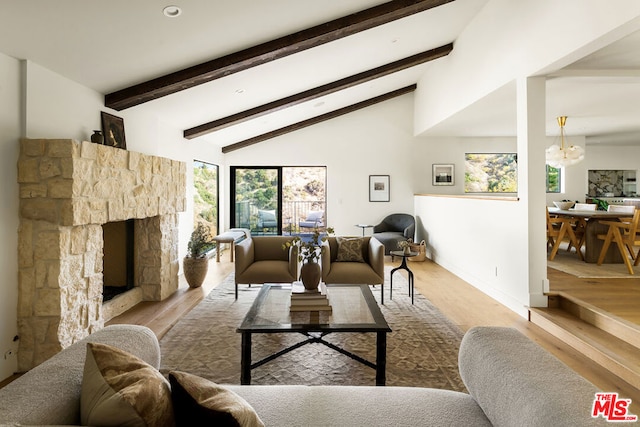 living room featuring light hardwood / wood-style floors, beamed ceiling, a stone fireplace, and a healthy amount of sunlight