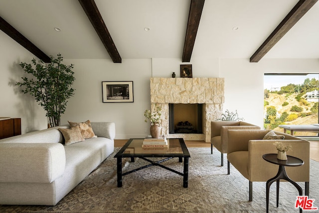 living room featuring wood-type flooring, a stone fireplace, and beamed ceiling