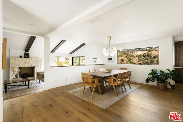 dining space with lofted ceiling with beams, a stone fireplace, a chandelier, and hardwood / wood-style floors