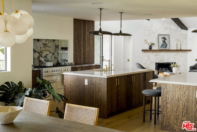 kitchen with a stone fireplace, sink, kitchen peninsula, light wood-type flooring, and dark brown cabinets