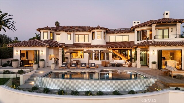 back house at dusk with a balcony and a patio