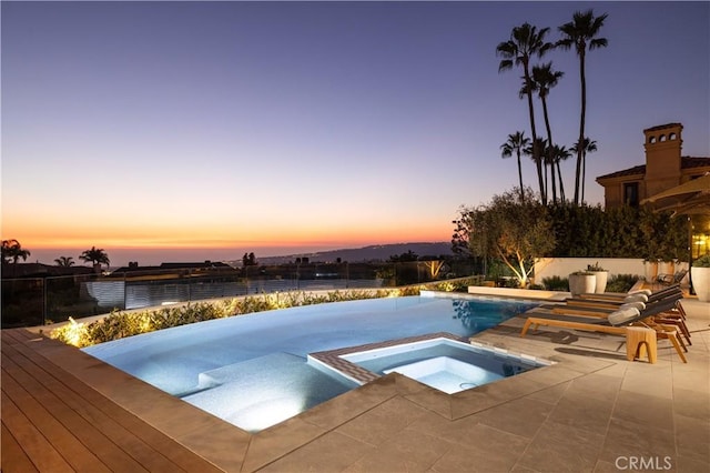 pool at dusk featuring an in ground hot tub