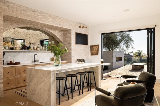 bar with a fireplace, light wood-type flooring, light stone countertops, and sink