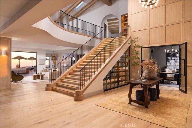 staircase with a high ceiling, beam ceiling, built in shelves, and wood-type flooring