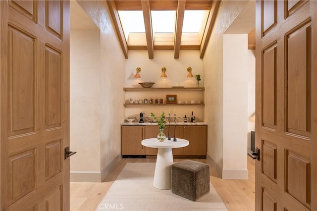 bar featuring lofted ceiling with skylight and light wood-type flooring