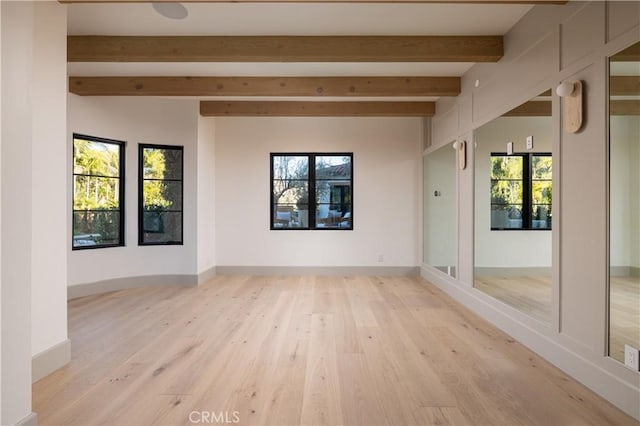 empty room with beam ceiling, light wood-type flooring, and plenty of natural light