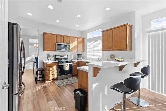 kitchen featuring a kitchen bar, appliances with stainless steel finishes, light hardwood / wood-style flooring, and kitchen peninsula