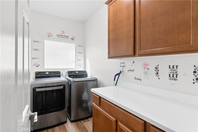 clothes washing area with light wood-type flooring, washing machine and clothes dryer, and cabinets