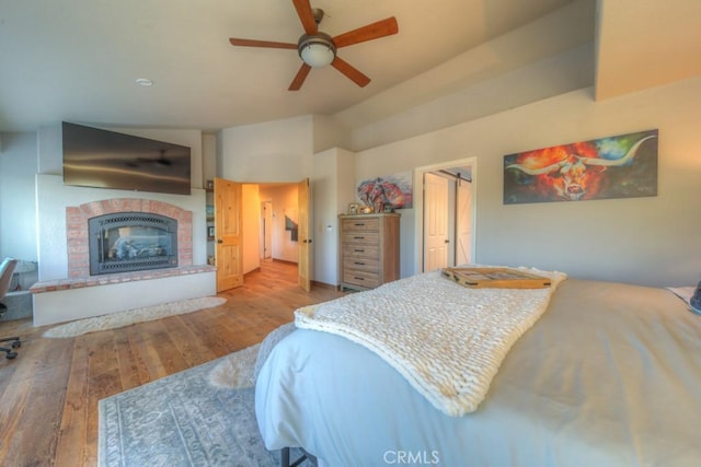 bedroom with lofted ceiling, a brick fireplace, ceiling fan, and light hardwood / wood-style floors