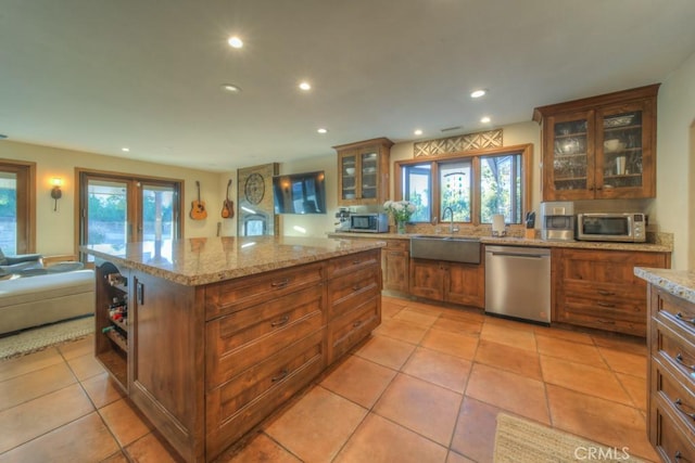 kitchen with light stone counters, a kitchen island, appliances with stainless steel finishes, light tile patterned flooring, and sink