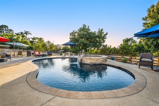 pool at dusk with pool water feature, an in ground hot tub, and a patio area