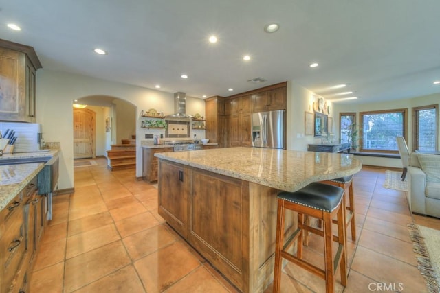 kitchen featuring light stone counters, a spacious island, stainless steel fridge with ice dispenser, and island exhaust hood