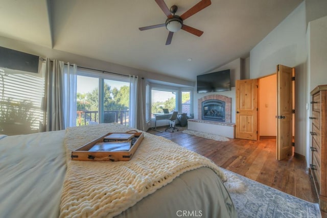 bedroom featuring access to outside, vaulted ceiling, a tile fireplace, ceiling fan, and wood-type flooring