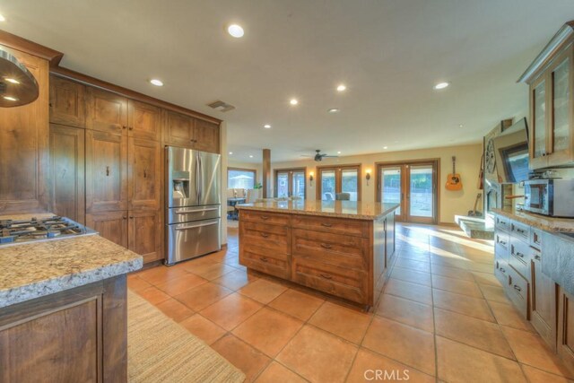 kitchen with appliances with stainless steel finishes, ceiling fan, light tile patterned floors, and a center island