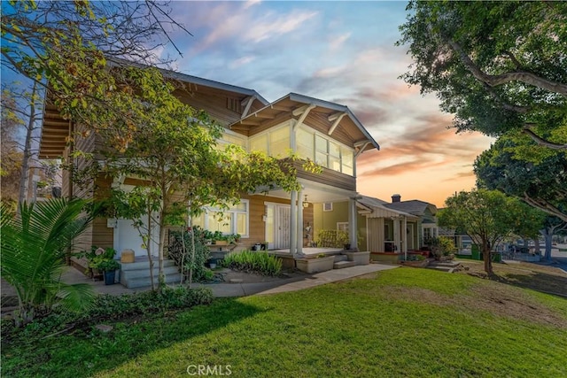 back house at dusk with covered porch and a lawn