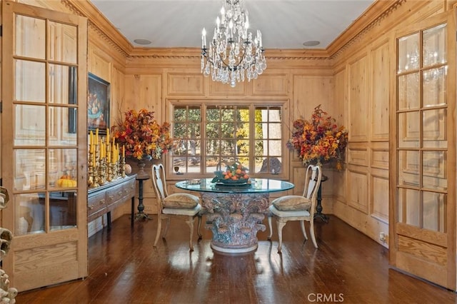 dining area featuring dark hardwood / wood-style floors, crown molding, a notable chandelier, and wooden walls