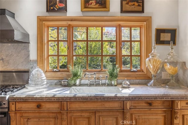 interior details featuring stainless steel range, light stone countertops, sink, and wall chimney range hood