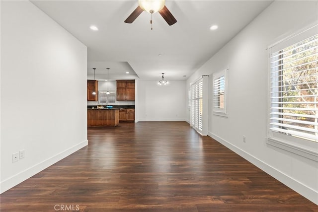 unfurnished living room featuring ceiling fan with notable chandelier and dark wood-type flooring