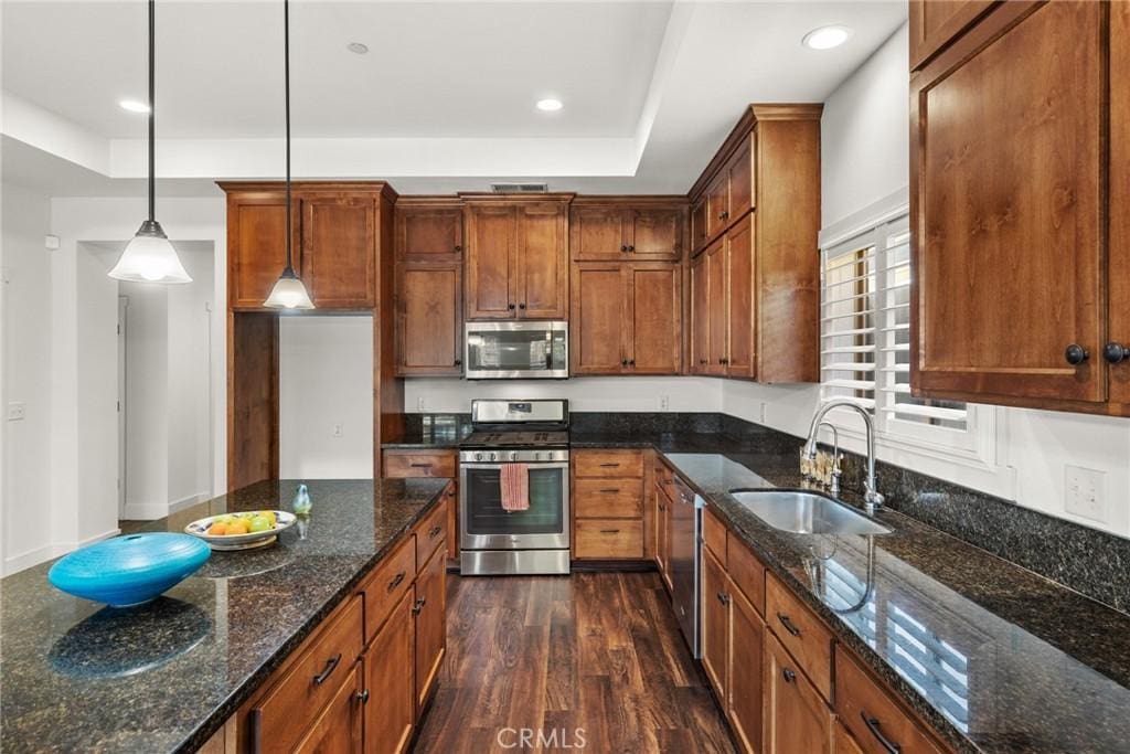 kitchen featuring appliances with stainless steel finishes, decorative light fixtures, dark wood-type flooring, dark stone countertops, and sink