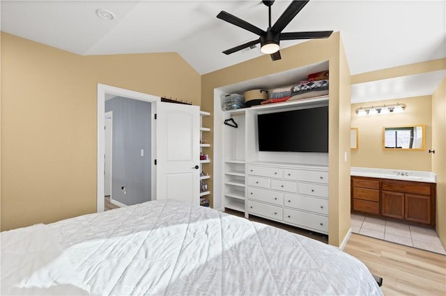 bedroom featuring ensuite bathroom, light hardwood / wood-style floors, ceiling fan, vaulted ceiling, and sink