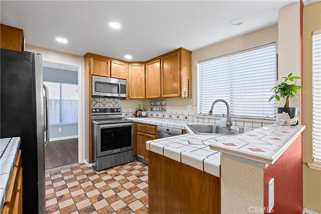 kitchen featuring appliances with stainless steel finishes, sink, backsplash, kitchen peninsula, and tile countertops