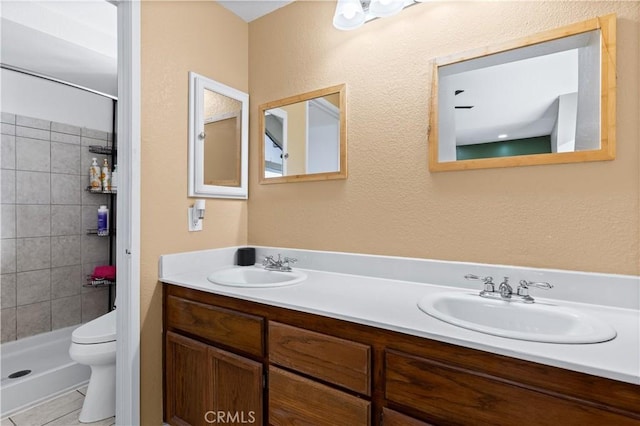 bathroom featuring toilet, vanity, tiled shower, and tile patterned flooring