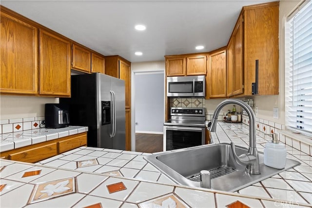 kitchen with appliances with stainless steel finishes, a wealth of natural light, tile counters, and sink