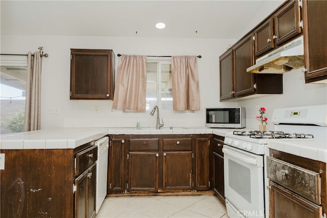 kitchen with white appliances, dark brown cabinetry, tile counters, sink, and kitchen peninsula