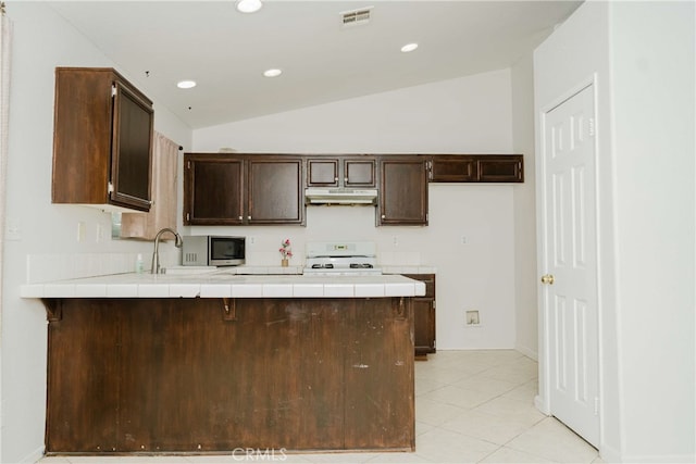 kitchen with tile counters, lofted ceiling, sink, and range