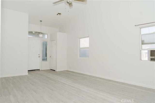 empty room with high vaulted ceiling, ceiling fan with notable chandelier, and light wood-type flooring