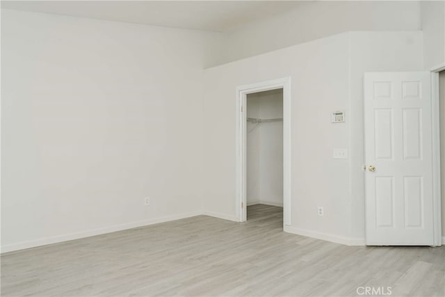 unfurnished bedroom with a spacious closet, a closet, and light hardwood / wood-style flooring