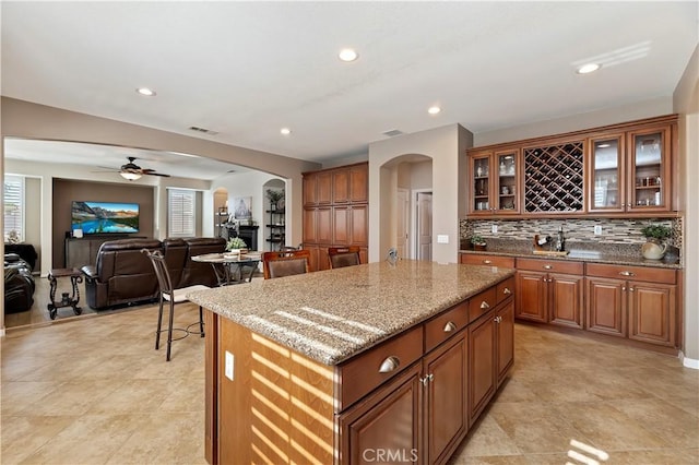 kitchen with light stone countertops, ceiling fan, decorative backsplash, and a kitchen island