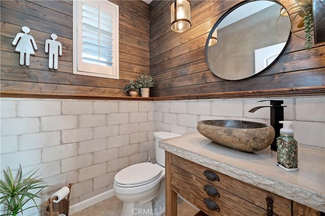 bathroom featuring toilet, wooden walls, and vanity