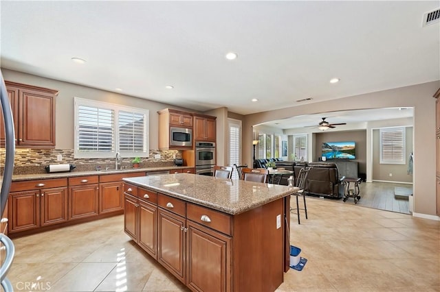 kitchen featuring stainless steel appliances, ceiling fan, light stone counters, a kitchen island, and sink