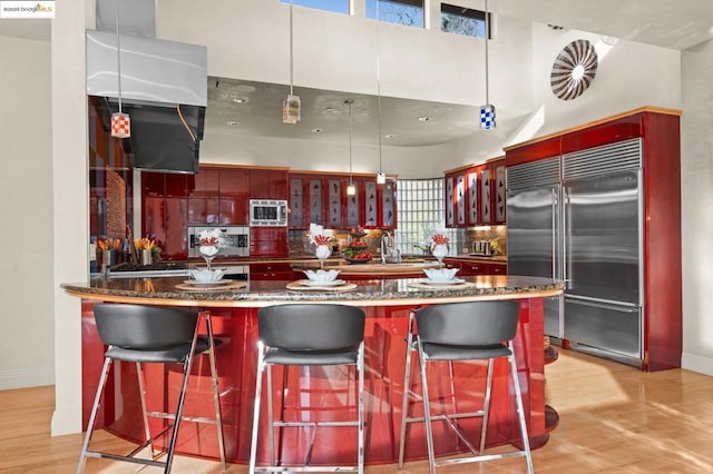 kitchen featuring sink, built in appliances, hanging light fixtures, a kitchen breakfast bar, and dark stone counters