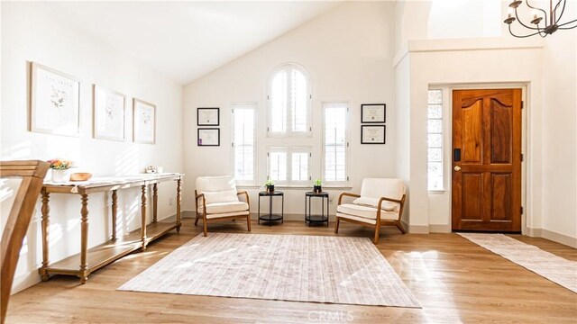 sitting room with high vaulted ceiling, wood-type flooring, and a notable chandelier