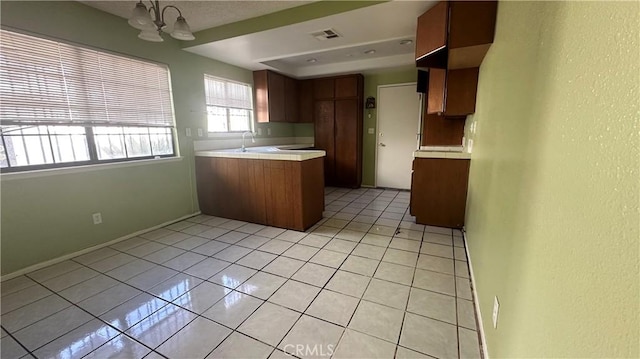 kitchen with sink, light tile patterned floors, kitchen peninsula, and an inviting chandelier