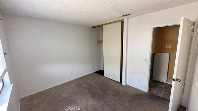 unfurnished bedroom with a closet, dark carpet, and a textured ceiling