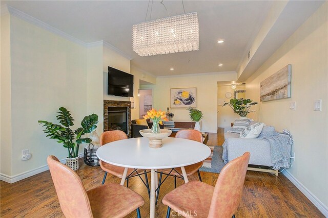 dining room with dark wood-type flooring, a chandelier, ornamental molding, and a stone fireplace