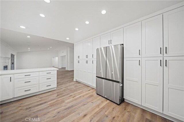 kitchen with white cabinets, light hardwood / wood-style flooring, crown molding, and stainless steel refrigerator