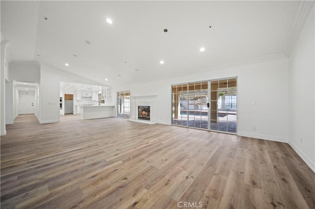 unfurnished living room with vaulted ceiling, ornamental molding, and light hardwood / wood-style flooring