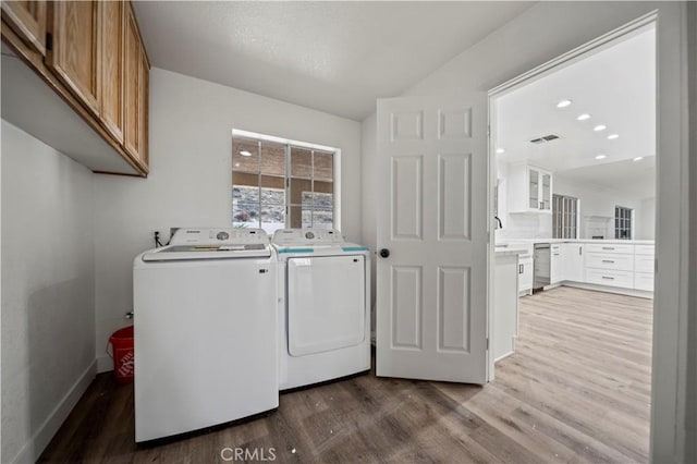 clothes washing area featuring wood-type flooring, independent washer and dryer, and cabinets