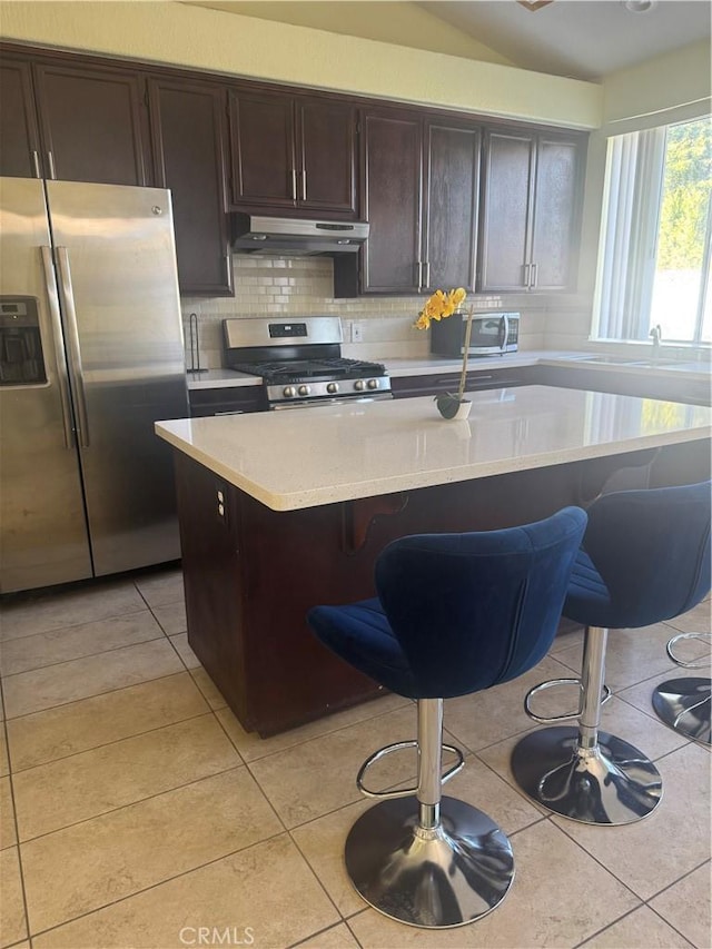 kitchen featuring light tile patterned floors, a kitchen bar, stainless steel appliances, and a center island