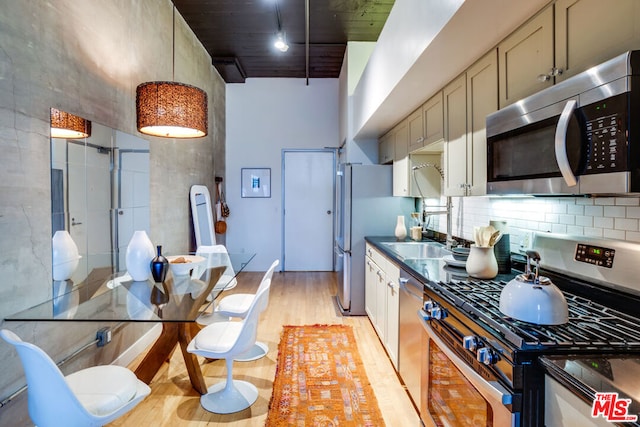 kitchen featuring a high ceiling, appliances with stainless steel finishes, sink, backsplash, and light hardwood / wood-style flooring