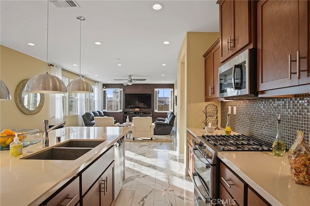 kitchen with ceiling fan, appliances with stainless steel finishes, decorative backsplash, hanging light fixtures, and sink