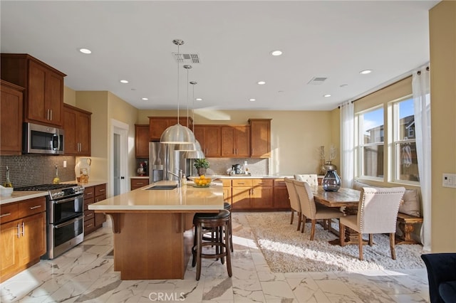 kitchen with pendant lighting, appliances with stainless steel finishes, decorative backsplash, a breakfast bar, and a center island with sink