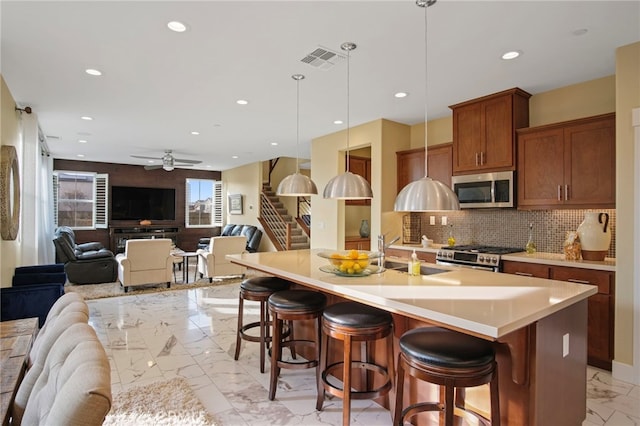 kitchen with a breakfast bar area, stainless steel appliances, a large island with sink, and hanging light fixtures