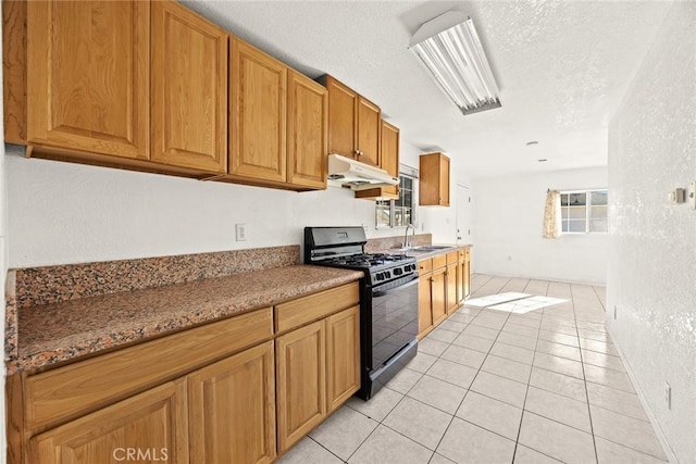 kitchen featuring gas stove, sink, light tile patterned flooring, a textured ceiling, and light stone counters