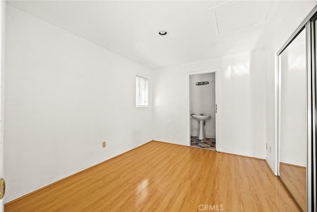 unfurnished bedroom with ensuite bathroom and light wood-type flooring