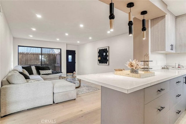 kitchen with light wood-type flooring, light stone countertops, white cabinetry, and decorative light fixtures